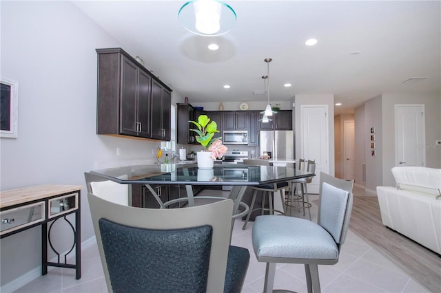 kitchen with appliances with stainless steel finishes, dark brown cabinets, light tile patterned floors, and decorative light fixtures