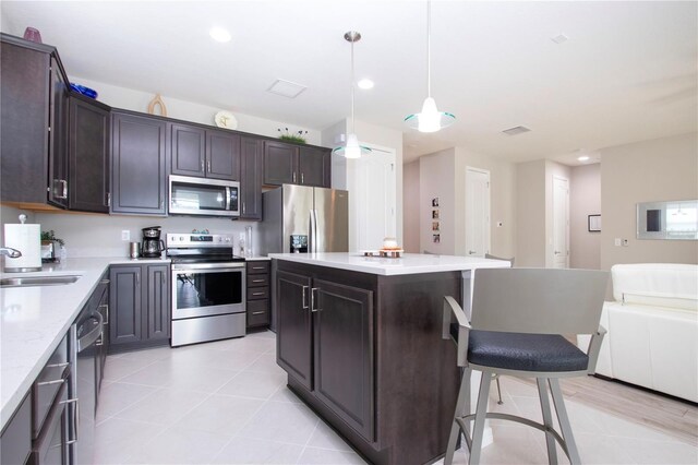 kitchen with decorative light fixtures, appliances with stainless steel finishes, a center island, sink, and dark brown cabinetry