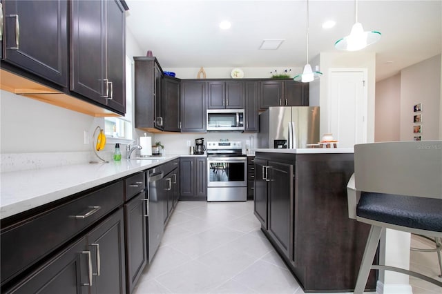 kitchen featuring pendant lighting, light stone counters, sink, appliances with stainless steel finishes, and dark brown cabinetry