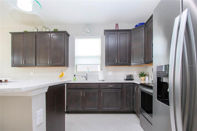 kitchen featuring appliances with stainless steel finishes, light tile patterned floors, dark brown cabinets, and sink