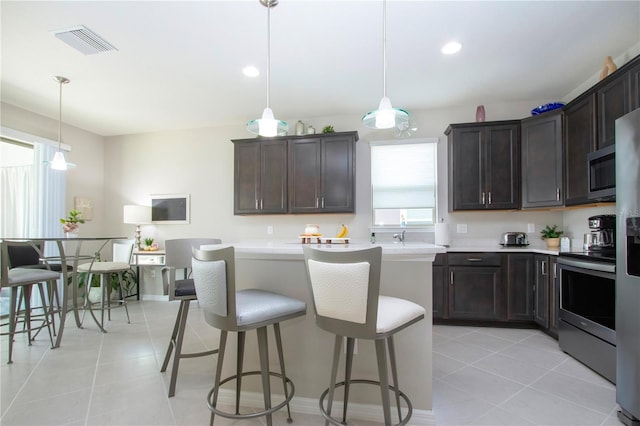 kitchen with stainless steel appliances, decorative light fixtures, a breakfast bar, light tile patterned flooring, and dark brown cabinetry