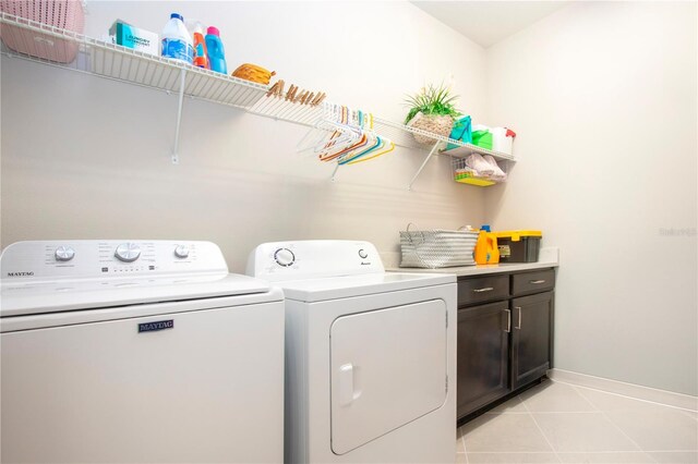 clothes washing area with washing machine and dryer, cabinets, and light tile patterned flooring