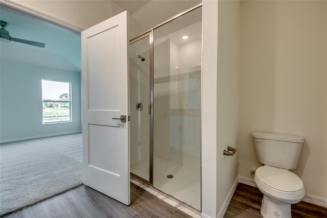 bathroom with toilet, ceiling fan, a shower stall, wood finished floors, and baseboards