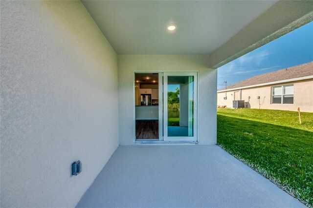 property entrance featuring a yard, central AC unit, a patio area, and stucco siding