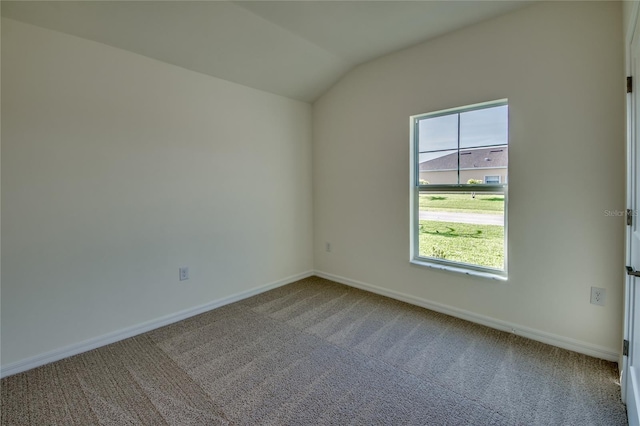 carpeted spare room featuring baseboards and vaulted ceiling