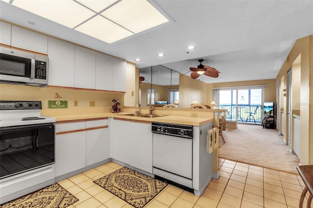 kitchen featuring white appliances, kitchen peninsula, light colored carpet, ceiling fan, and white cabinets