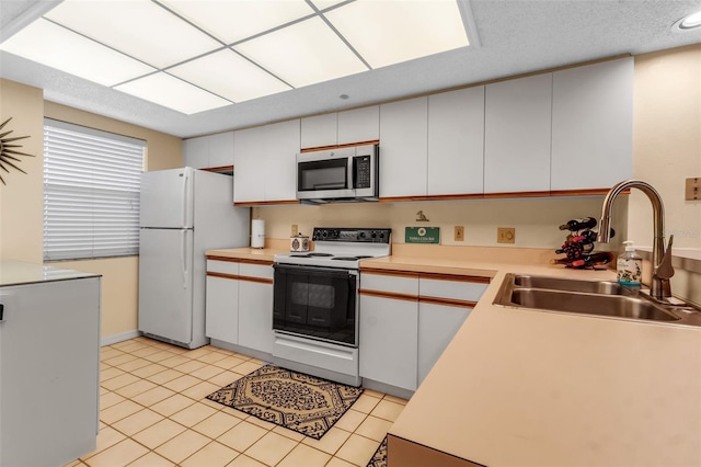 kitchen with sink, white appliances, white cabinets, and light tile patterned flooring