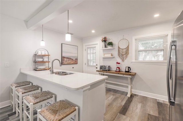 kitchen with stainless steel refrigerator, sink, wood-type flooring, kitchen peninsula, and pendant lighting