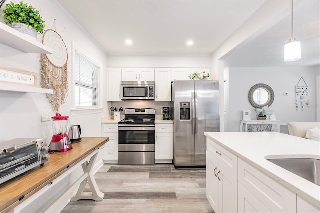 kitchen with light wood-type flooring, stainless steel appliances, white cabinetry, pendant lighting, and tasteful backsplash