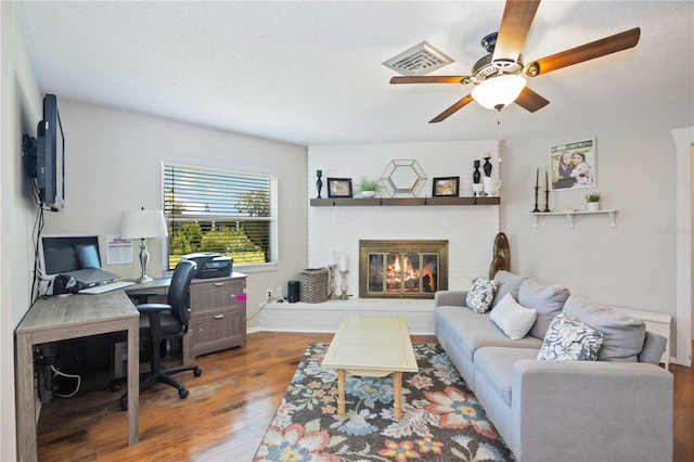 office space featuring ceiling fan, a textured ceiling, wood-type flooring, and a brick fireplace