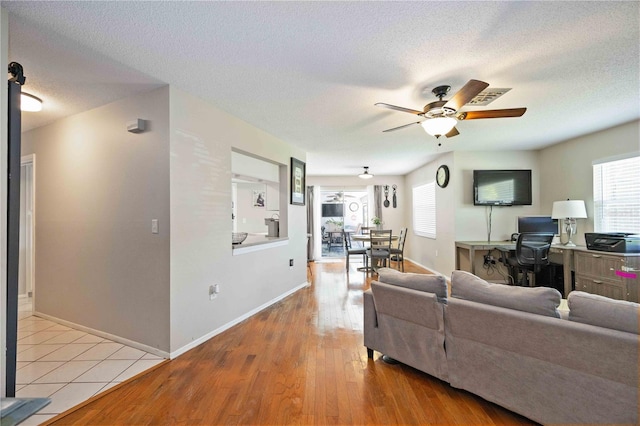 living room with a textured ceiling, ceiling fan, and light hardwood / wood-style floors