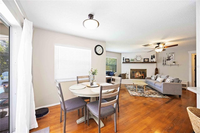 dining space with wood-type flooring, ceiling fan, and a brick fireplace