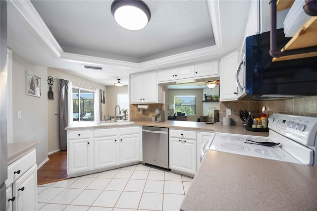 kitchen with a tray ceiling, white electric range, stainless steel dishwasher, kitchen peninsula, and white cabinets