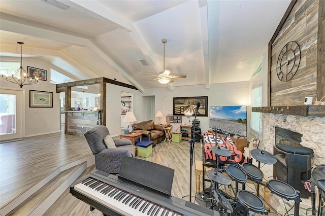 living room featuring ceiling fan with notable chandelier, wood-type flooring, lofted ceiling with beams, and a stone fireplace