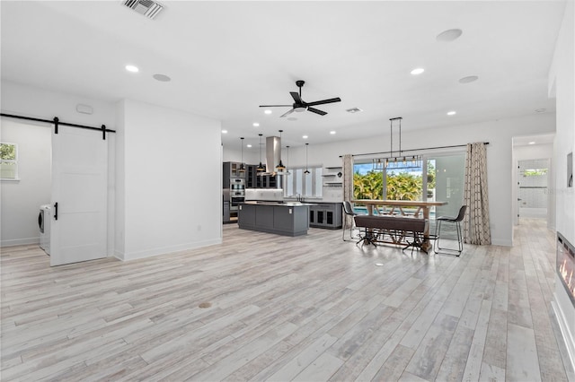 living room featuring ceiling fan, light hardwood / wood-style floors, a barn door, and washing machine and clothes dryer