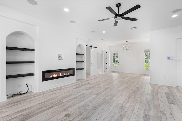 unfurnished living room featuring built in shelves, ceiling fan, a barn door, and light hardwood / wood-style floors