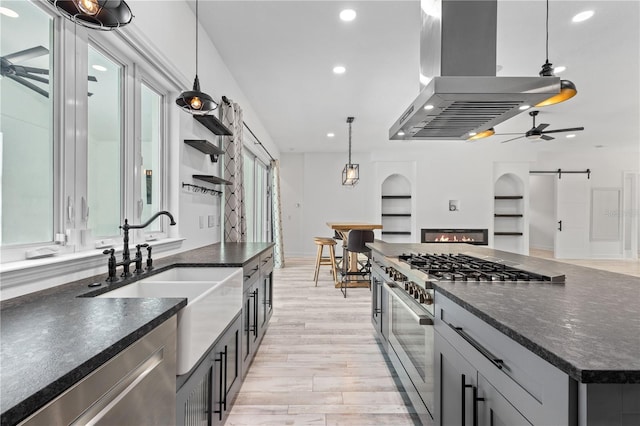 kitchen featuring island range hood, appliances with stainless steel finishes, built in features, pendant lighting, and a barn door