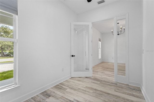 unfurnished room with ceiling fan with notable chandelier and light wood-type flooring