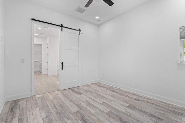 unfurnished room featuring light hardwood / wood-style floors, a barn door, and ceiling fan