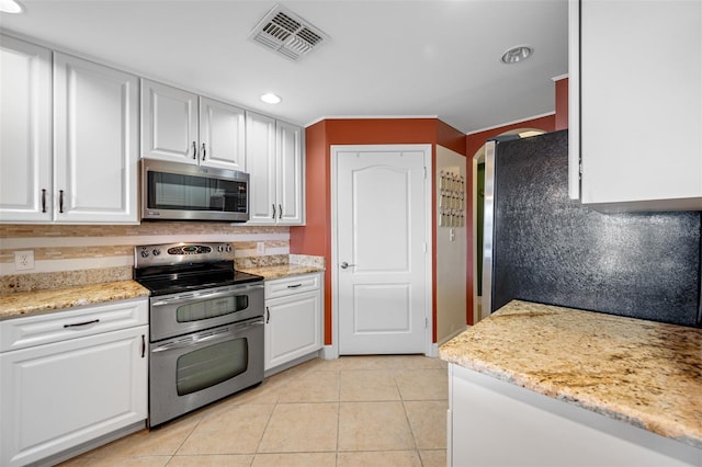 kitchen with light stone countertops, light tile patterned floors, backsplash, appliances with stainless steel finishes, and white cabinetry