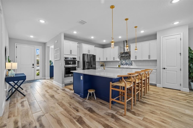 kitchen featuring white cabinets, appliances with stainless steel finishes, wall chimney exhaust hood, a kitchen breakfast bar, and a kitchen island with sink