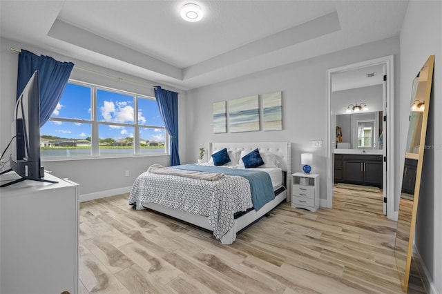 bedroom with light wood-type flooring, a raised ceiling, connected bathroom, and sink