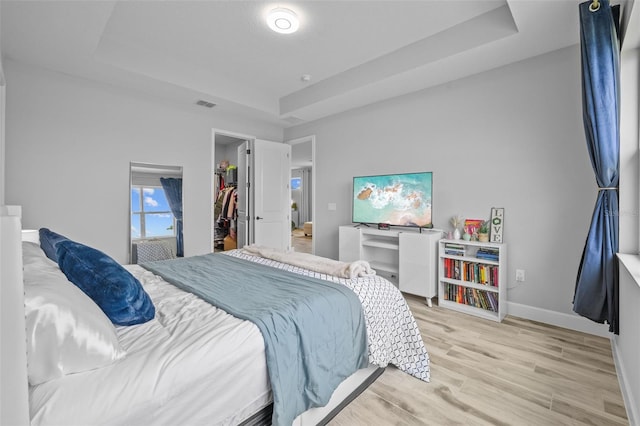 bedroom with light hardwood / wood-style flooring, a raised ceiling, a spacious closet, and a closet