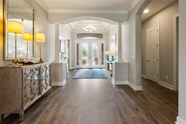 foyer entrance with a raised ceiling, an inviting chandelier, ornate columns, crown molding, and dark wood-type flooring