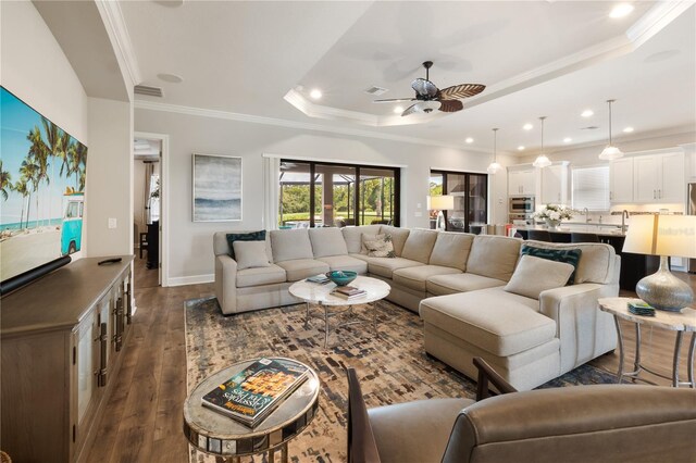 living room with ornamental molding, dark wood-type flooring, a raised ceiling, and ceiling fan