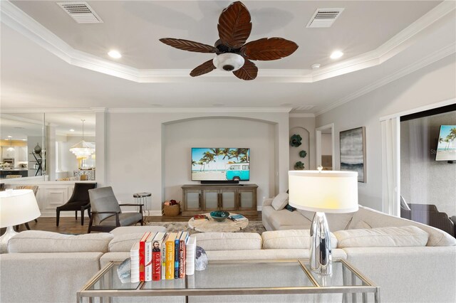 living room with ceiling fan, hardwood / wood-style flooring, a raised ceiling, and ornamental molding