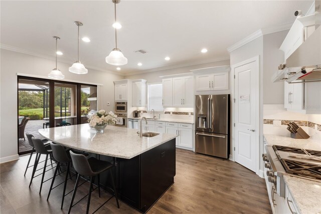 kitchen featuring dark hardwood / wood-style floors, range hood, appliances with stainless steel finishes, a kitchen island with sink, and white cabinetry