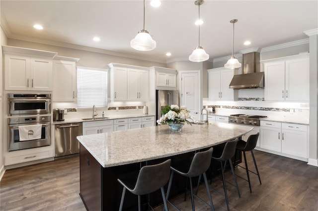 kitchen featuring stainless steel appliances, sink, dark wood-type flooring, wall chimney exhaust hood, and a center island with sink