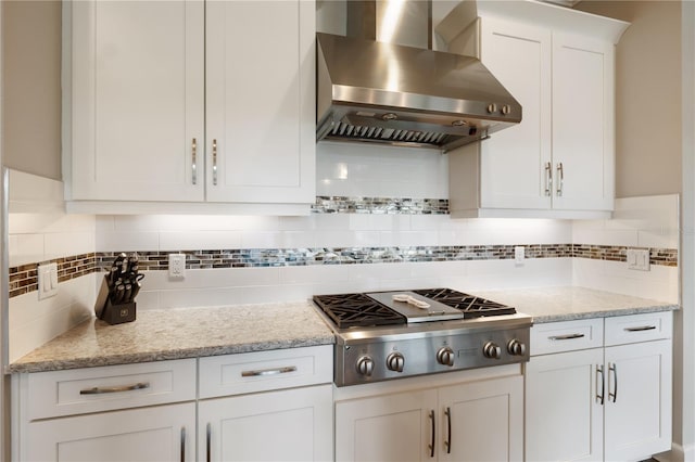 kitchen with white cabinets, stainless steel gas stovetop, light stone counters, wall chimney exhaust hood, and decorative backsplash