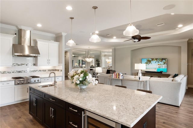 kitchen featuring stainless steel gas stovetop, sink, wall chimney range hood, dark hardwood / wood-style floors, and ceiling fan