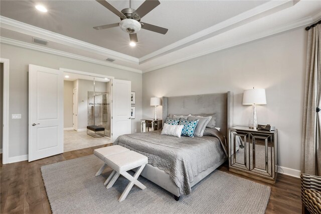 bedroom with ornamental molding, dark hardwood / wood-style flooring, ceiling fan, a tray ceiling, and ensuite bathroom