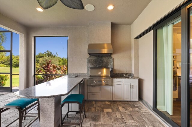 kitchen featuring white cabinetry, kitchen peninsula, sink, ceiling fan, and wall chimney range hood