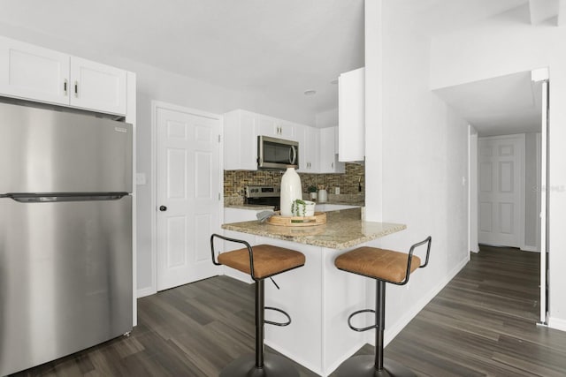 kitchen with a kitchen breakfast bar, white cabinetry, kitchen peninsula, and appliances with stainless steel finishes