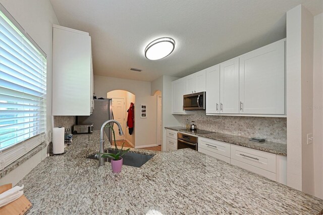 kitchen with light stone countertops, tasteful backsplash, stainless steel appliances, sink, and white cabinetry