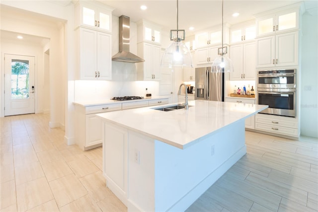 kitchen featuring pendant lighting, an island with sink, stainless steel appliances, sink, and wall chimney range hood