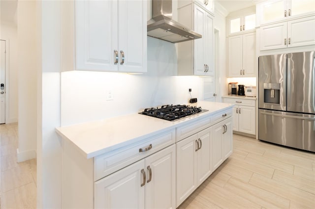 kitchen with black gas stovetop, stainless steel fridge, wall chimney exhaust hood, and white cabinetry