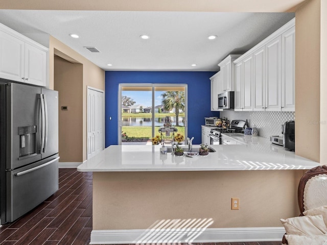 kitchen with backsplash, stainless steel appliances, kitchen peninsula, dark hardwood / wood-style floors, and white cabinetry