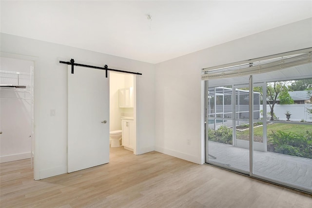 unfurnished bedroom with access to exterior, a barn door, connected bathroom, a closet, and light wood-type flooring