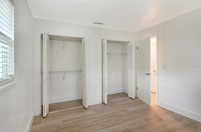 unfurnished bedroom with visible vents, baseboards, light wood-style floors, and multiple closets