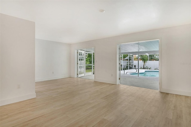 empty room with light wood-type flooring, baseboards, a healthy amount of sunlight, and a sunroom