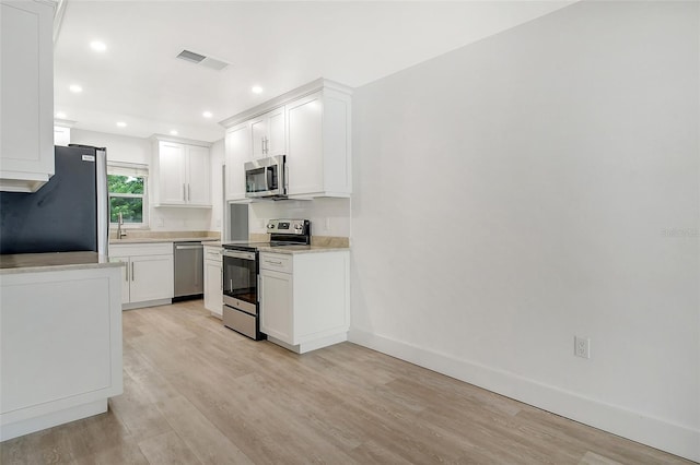 kitchen with appliances with stainless steel finishes, white cabinets, light wood finished floors, baseboards, and light countertops