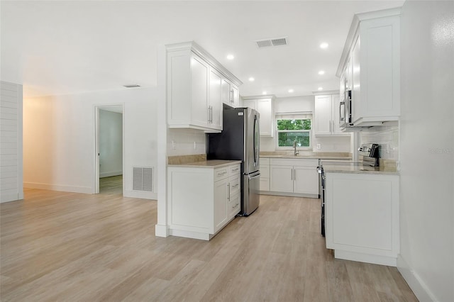 kitchen with stainless steel appliances, white cabinets, decorative backsplash, sink, and light hardwood / wood-style flooring