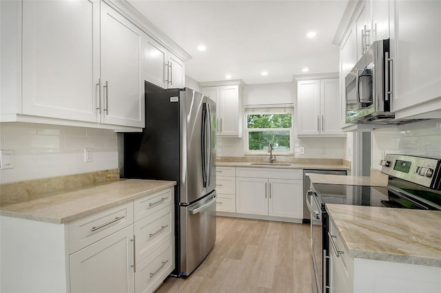 kitchen with a sink, stainless steel appliances, light wood finished floors, and white cabinetry