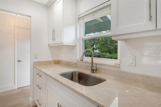 kitchen with white cabinetry, sink, light wood-type flooring, and light stone counters