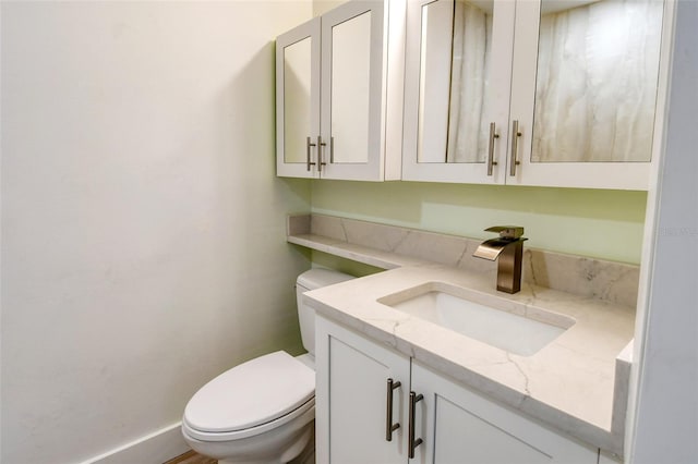 half bathroom with vanity, toilet, and baseboards