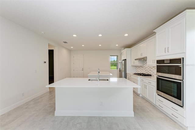 kitchen featuring stainless steel appliances, sink, white cabinetry, and a kitchen island with sink